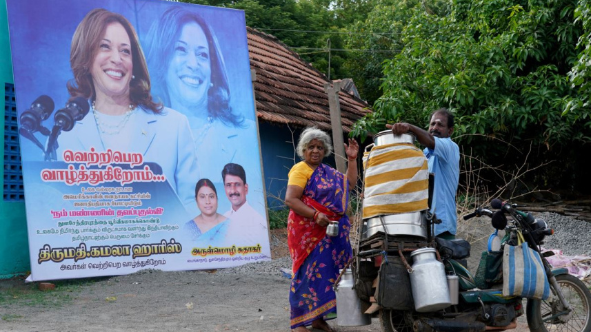তামিলনাড়ুর গ্রাম থুলাসেন্দ্রাপুরামে ১০০ বছর আগে কমলা হ্যারিসের নানা জন্ম নিয়েছিলেন। এই গ্রামে তার নির্বাচনী প্রচারণা সম্বলিত বিলবোর্ডের সামনে দাঁড়িয়ে দুধ কিনছেন এক নারী। ছবি: রয়টার্স