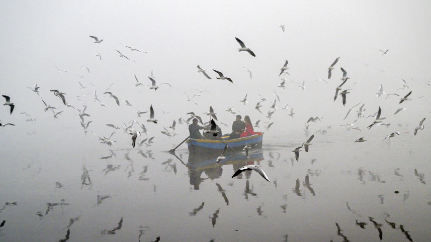 ঘন কুয়াশার মাঝে যমুনা নদীতে পাখিদের খাবার দিচ্ছেন দিল্লিবাসীরা। ছবি: এএফপি