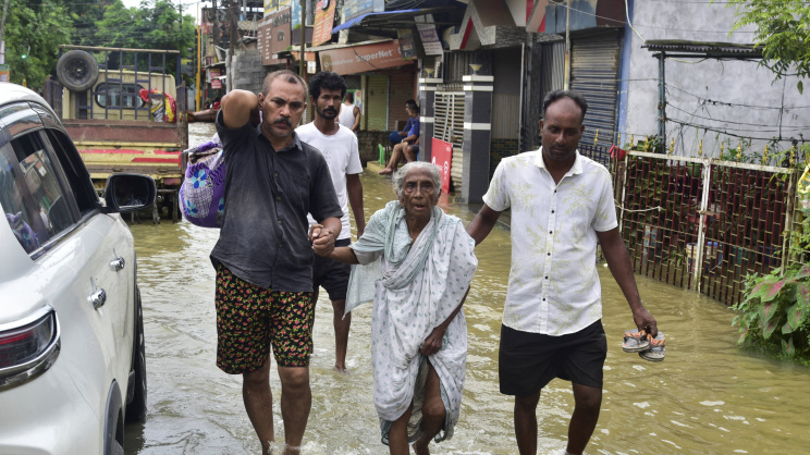 শিবসাগর জেলায় বন্যাকবলিত এলাকায় এক বৃদ্ধাকে অন্যান্যরা সাহায্য করছেন। ছবি: রয়টার্স