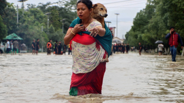 ভারতের মণিপুর রাজ্যের রাজধানী ইমফালে এক নারী বন্যার হাত থেকে নিজেকে ও তার পোষা কুকুরকে রক্ষার চেষ্টা চালাচ্ছেন। ছবি: এএফপি (১ জুন, ২০২৫)
