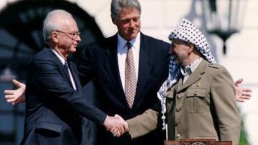 অসলো চুক্তিতে সই করার পর পিএলও চেয়ারম্যান ইয়াসির আরাফাতের সঙ্গে হাত মেলাচ্ছেন ইসরায়েলি প্রধানমন্ত্রী ইৎজাক রাবিন। তাদের মাঝে মার্কিন প্রেসিডেন্ট বিল ক্লিনটন। ফাইল ছবি: রয়টার্স (১৩ সেপ্টেম্বর, ১৯৯৩)  