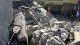 People stand in front of a damaged house that the Afghan Taliban government said was damaged after Pakistan carried out raids, in Asadabad, Kunar province, Afghanistan, November 25, 2025/ Reuters